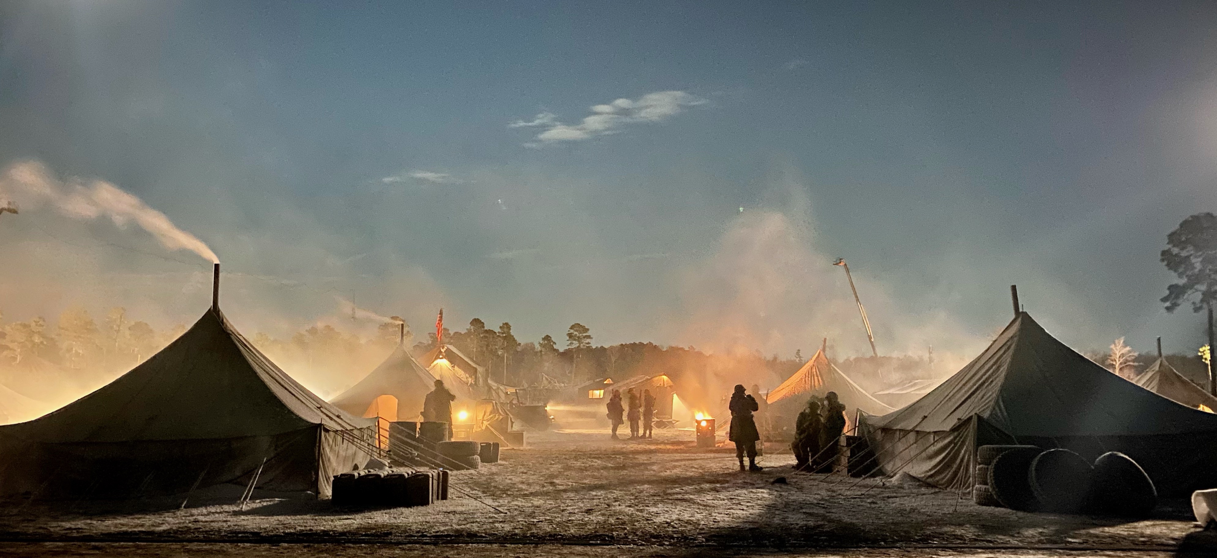 Photo of film set at dusk with tents, people and a small fire